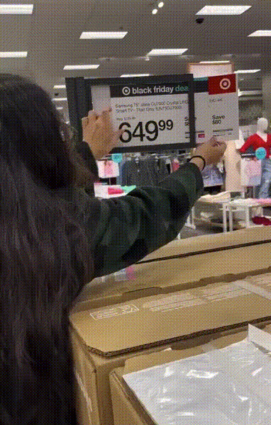 woman at target store pulls out the product sale price sign that's covered by the black friday deals